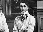 Portrait of young woman with coifed hair, high necked dress with flouncy necktie.