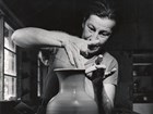 Woman concentrates, using tips of fingers to carefully finish rim on clay pot.