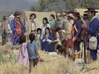 Group of Latino mourners surround deceased woman in arid landscape