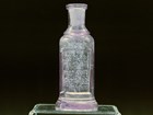 Small glass bottle with enscription sits on acrylic stand.