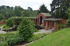 A brick pool house and pergola in a formal garden, beside a pond, garden beds, and terracing