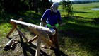 SCA intern uses an axe to shape the end of a log, held in place in a rustic sawhorse. 