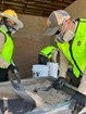 Workers are shoveling coarse sand onto a mesh screen. 