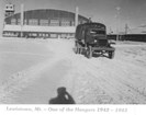 Black and white photo of a truck in front of airplane hangar 