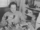 Historic black and white photo of an artist sculpting a model of an animal.