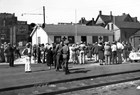 Black and white photo of crowd outside of a single story building