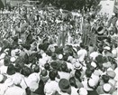 Black and white photo of three men on a stage above a large crowd