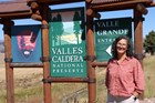 A woman stands in front of a colorful park entrance sign that says Valles Caldera National Preserve