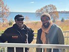 Two African American men stand infront of a blue body of water. 