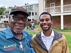 Two African American men take a selfie infront of buildings.