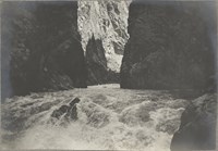 Rushing rapids between dark canyon walls. Sunlight is visible farther upstream.
