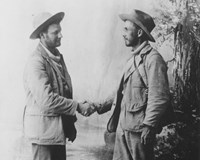Black and white drawing of two men shaking hands. They are wearing jackets and broad brim hats.