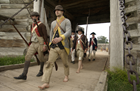Men walk quickly from the main gate of the fort carrying their muskets. 