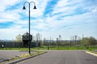 : A black lightpost, tall and with two hooks each holding a light, is shown in an empty parking lot.