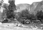 1920s model cars park around mature fruit trees and stones, with steep cliffs behind