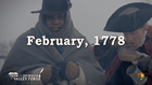 A man wrapped in a blanket on the left, another man spoons a steaming liquid into his mouth.