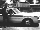 Photograph of a man in an NPS ranger uniform standing next to a patrol vehicle.