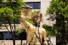 Gold toned statue of a man in a tri-corner hat holding up a scroll