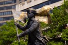 Dark bronze and gold toned statue of a man in a tri-corner hat waving a large American flag