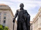 Dark bronze statue of a man holding a book, cloak, and saber