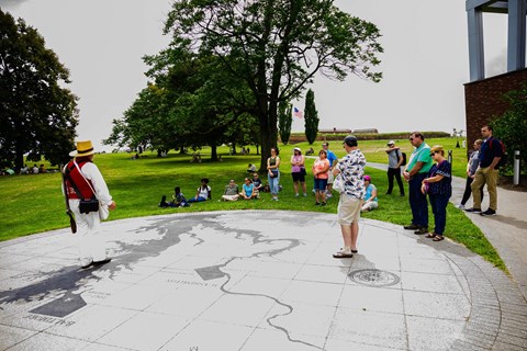 Volunteer in living history kit delivering program to visitors.