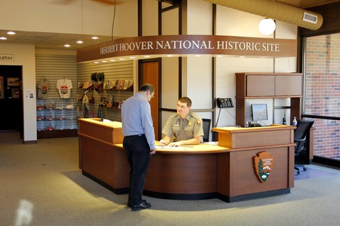 A uniformed ranger at an information desk assists a park visitor.
