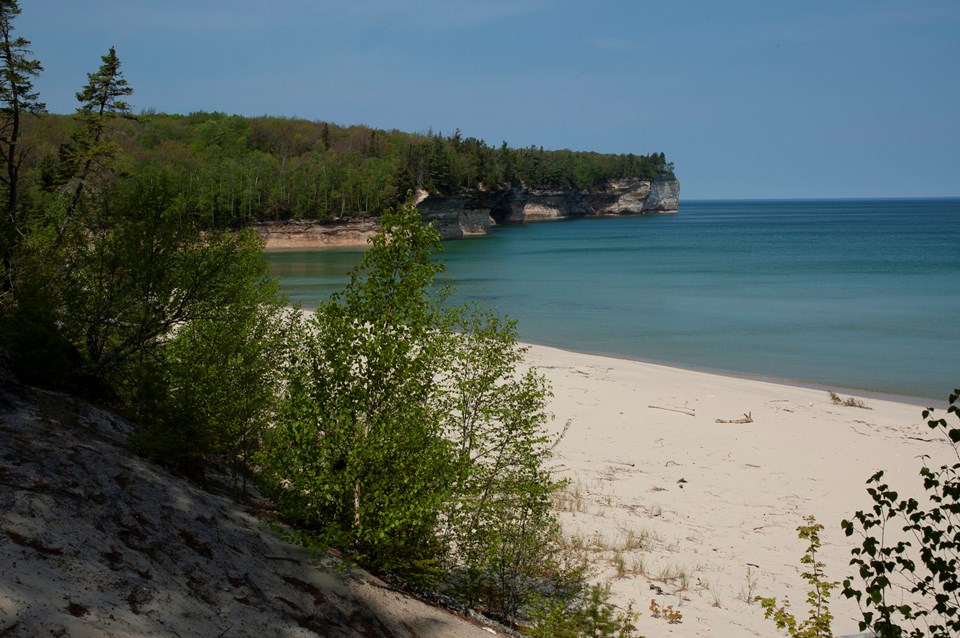 Small beach on Lake Superior. Rock cliffs rise out of the water in the distance. The water is calm.