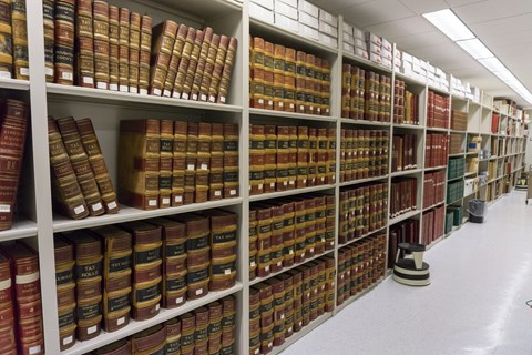 Tall bookcases line the length of the image, with white floors and flourescent lights