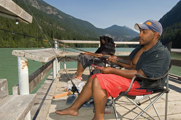 Two men sit fishing in chairs on a wooden pier