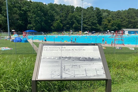 A wayside exhibit in the foreground of a large public pool.