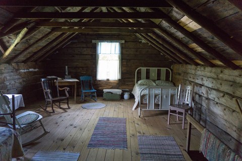Antique chairs and beds in an attic with a single window and exposed rafters