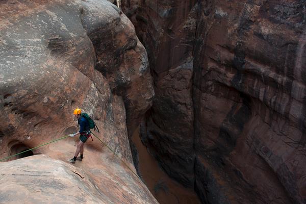 A person harnessed to a rope prepares to rappel into a canyon