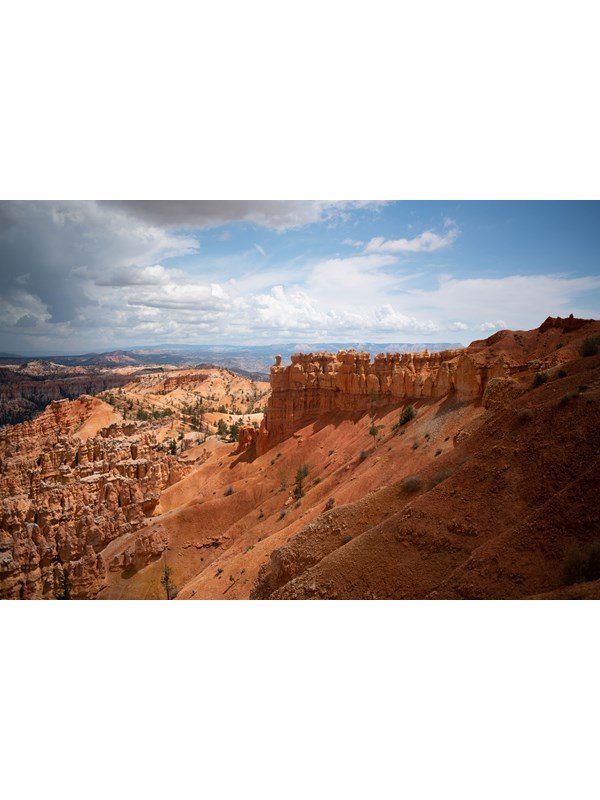 Red rock formations on top of a steep sandy slope with distant red rock formations in the background