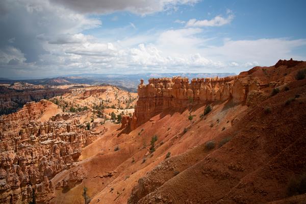 Red rock formations on top of a steep sandy slope with distant red rock formations in the background