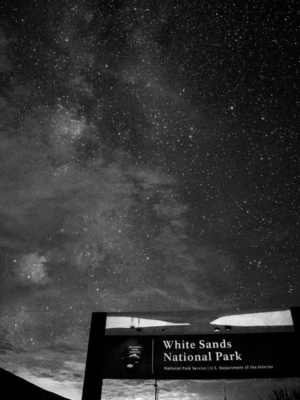 A sign reads "White Sands National Park" with a dark night sky with milky way in the background