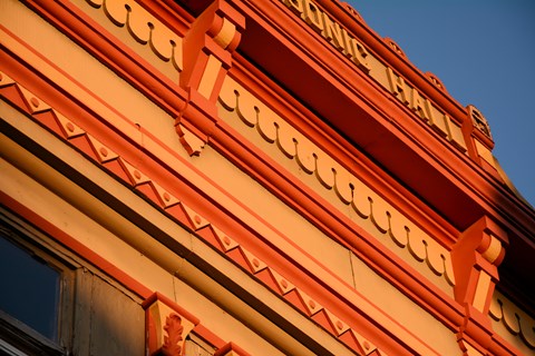 A detail photo of a building cornice shows courses of red and orange decorations.