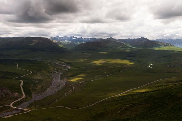 River and road with mountains in the background and a cloudy sky.