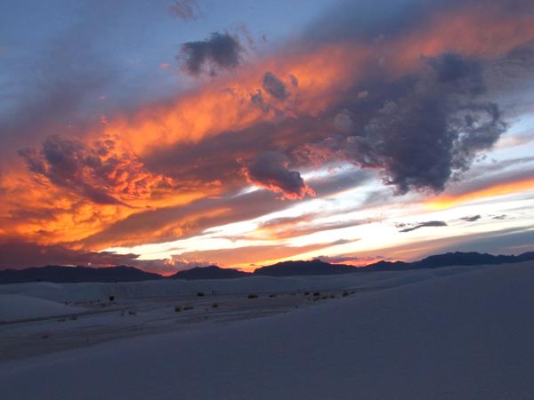 White sand dunes with mountains in the distance at sunset