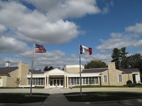 A sprawling one story public building of rough-faced yellowish stone has a white portico entrance.