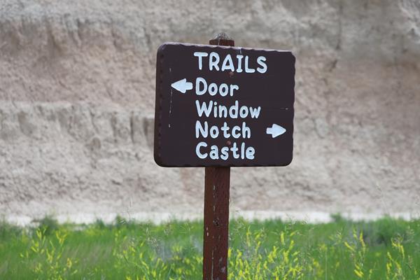 a brown sign with white writing points to door, window, notch, and castle trails.