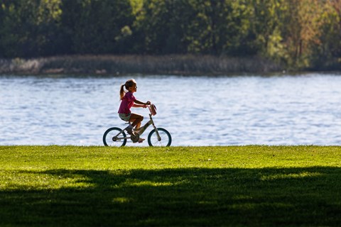 A young girl rides her bike in a grassy area along the river.