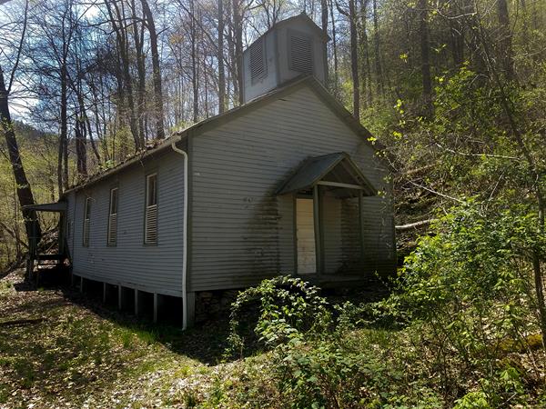 A blue sided church surrounded by the forest.