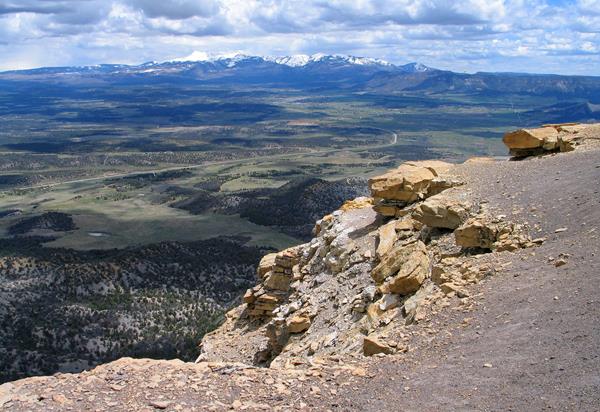 Overlooking a broad green valley with snow-capped mountains in the distance.