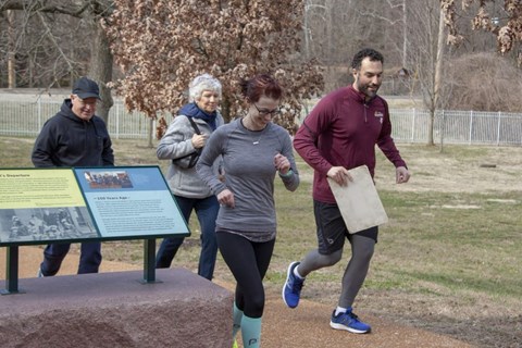 Four people in running gear lightly jogging on concrete with grass in the background.