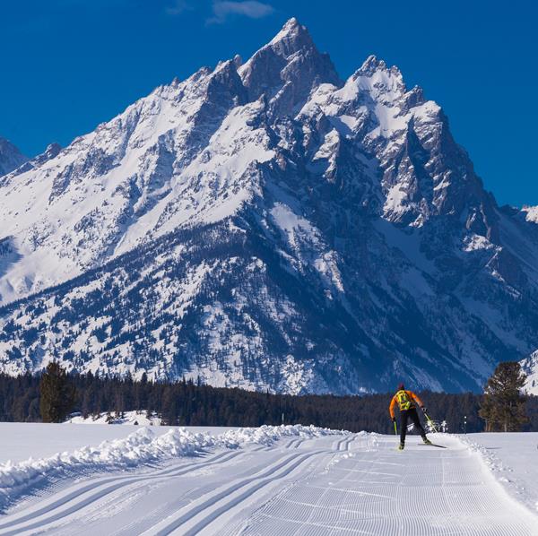 Skate skier on groomed Teton Park Road. Mountains rise in the distance.