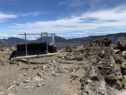 Rocky overlook area with a simple metal and glass structure on the edge of the crater.