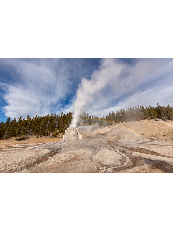 Steam and water erupt from the tan cone of Lone Star Geyser. A rainbow appears in the mist.