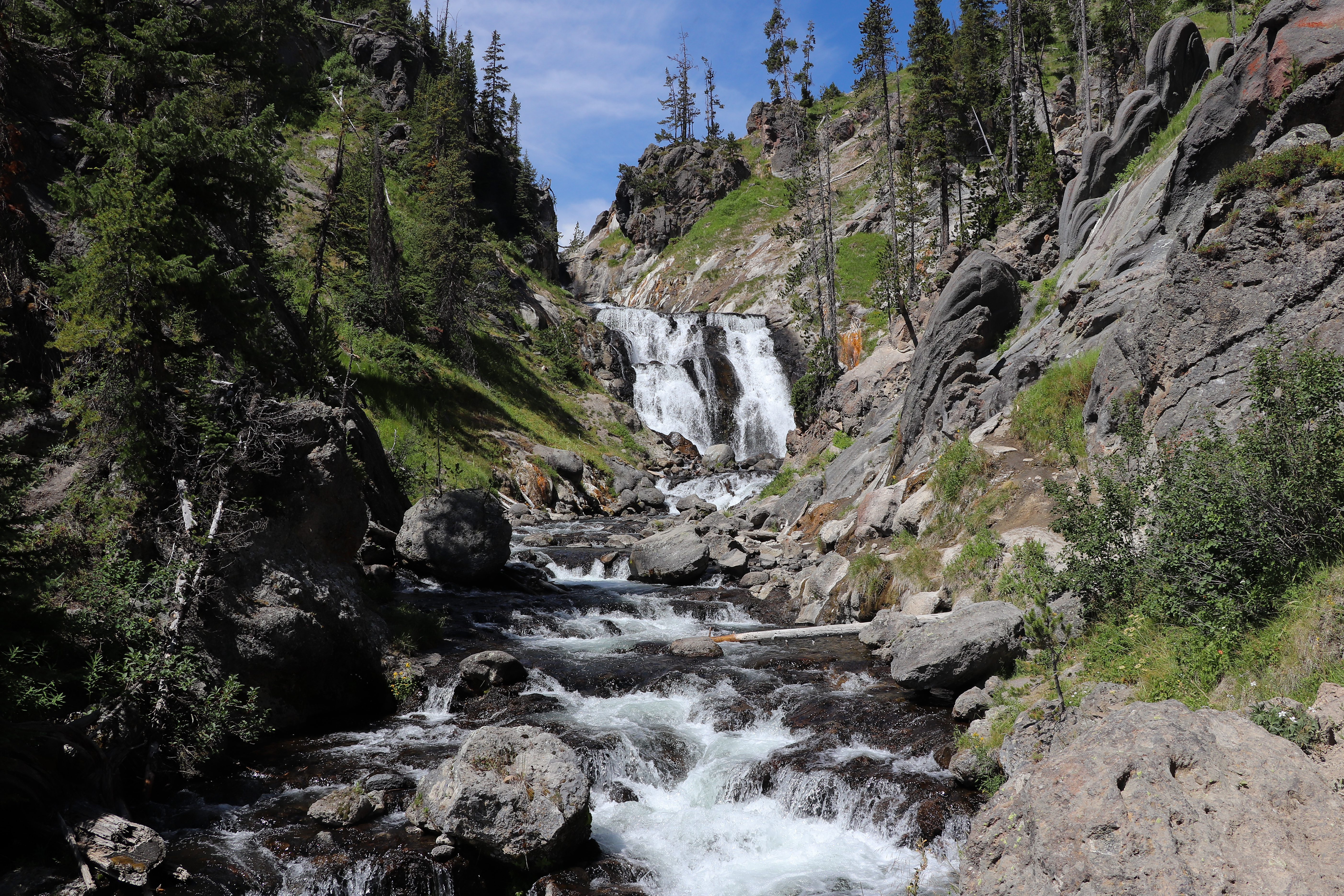 A waterfall cascades over a cliff and flows into a stream down a rocky creek.