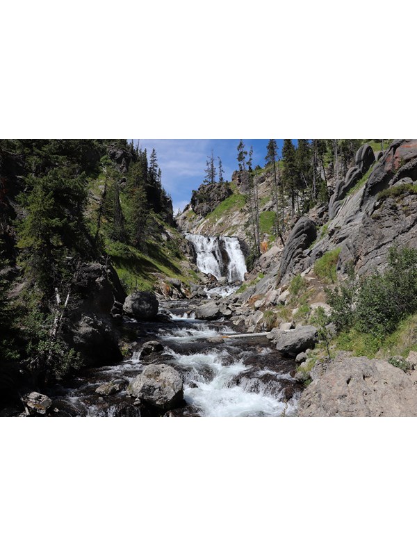 A waterfall cascades over a cliff and flows into a stream down a rocky creek.
