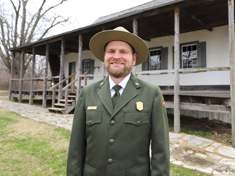 A smiling park ranger stands in front of a historic building